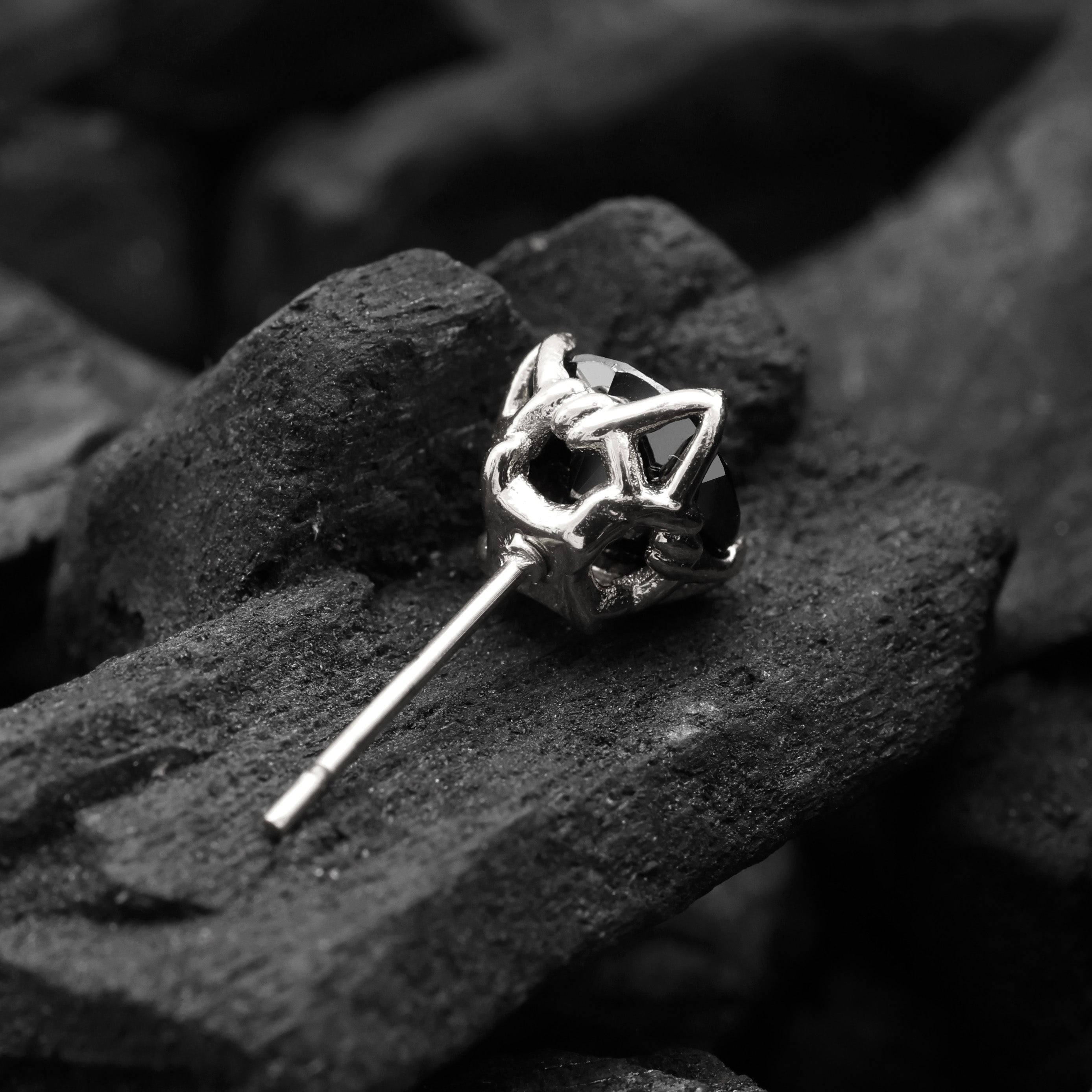 Silver stud earring on a dark stone surface