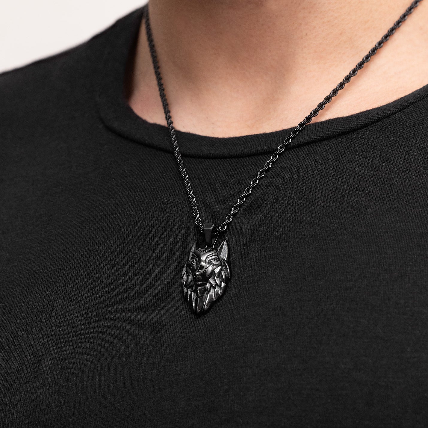 Wolf head pendant necklace on a black chain worn by a person against a black background