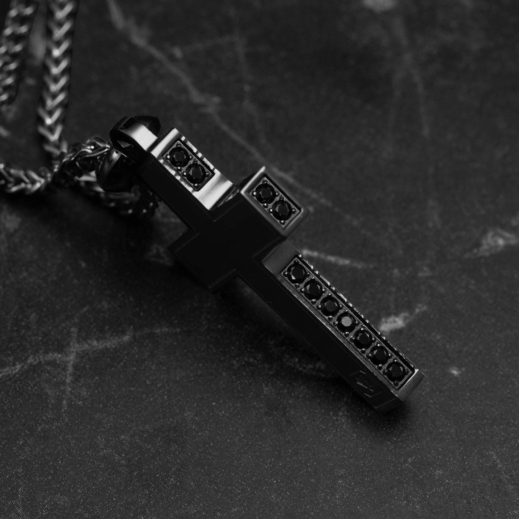 Black and silver cross pendant necklace on a dark surface