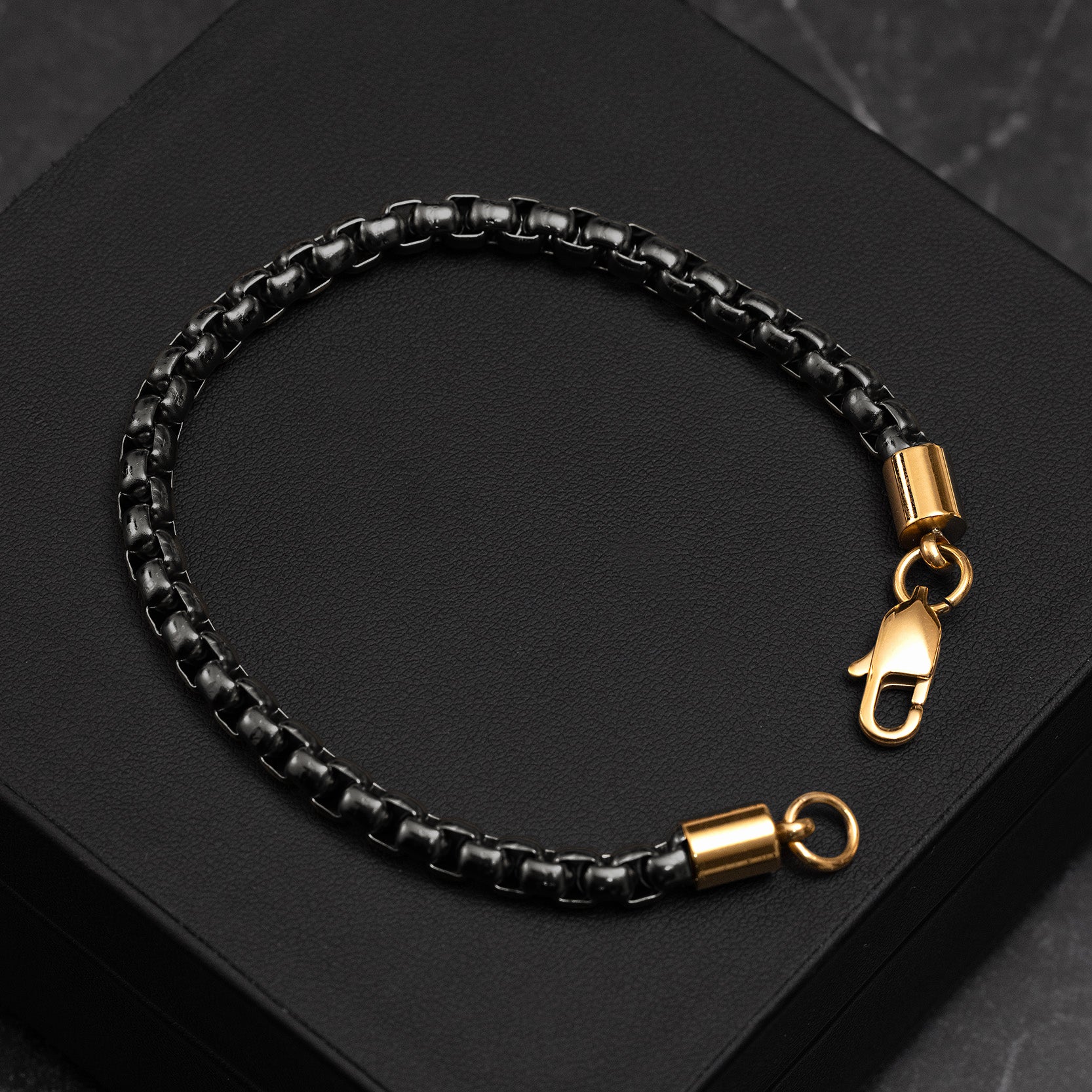 Black braided leather bracelet with gold clasp on a dark surface
