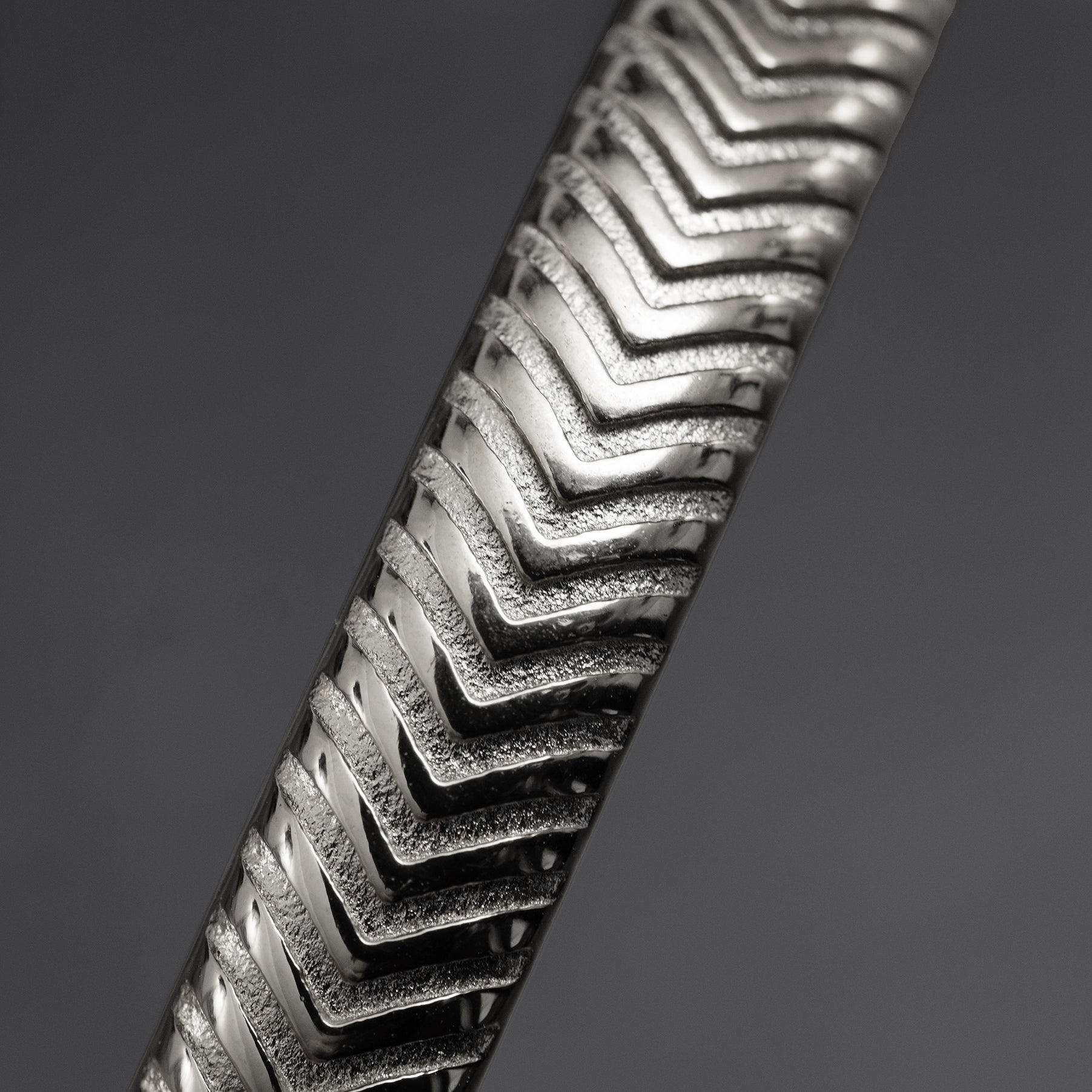 Close-up of a metallic bracelet with chevron pattern on a dark background