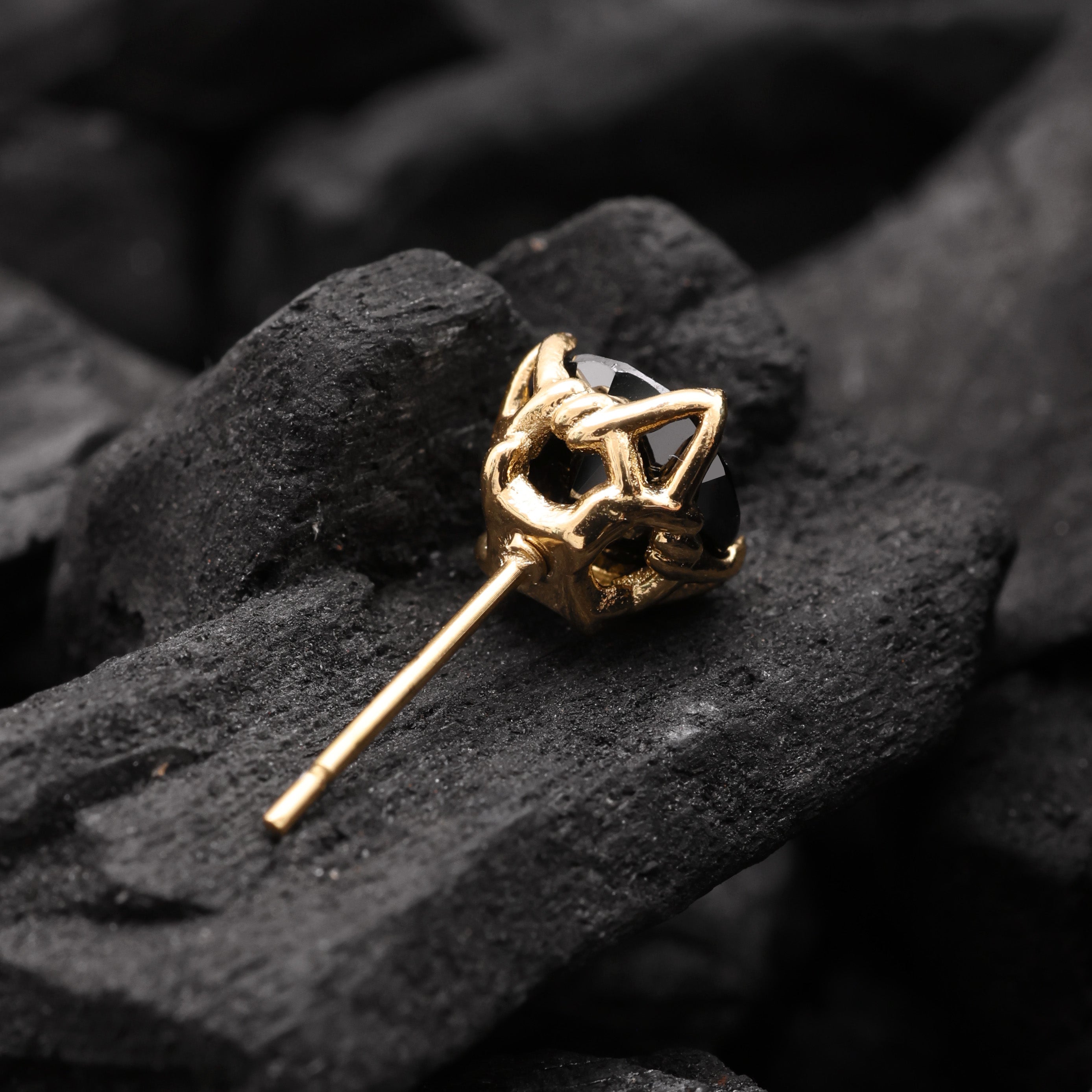 Gold earring with black gemstone on a dark stone surface