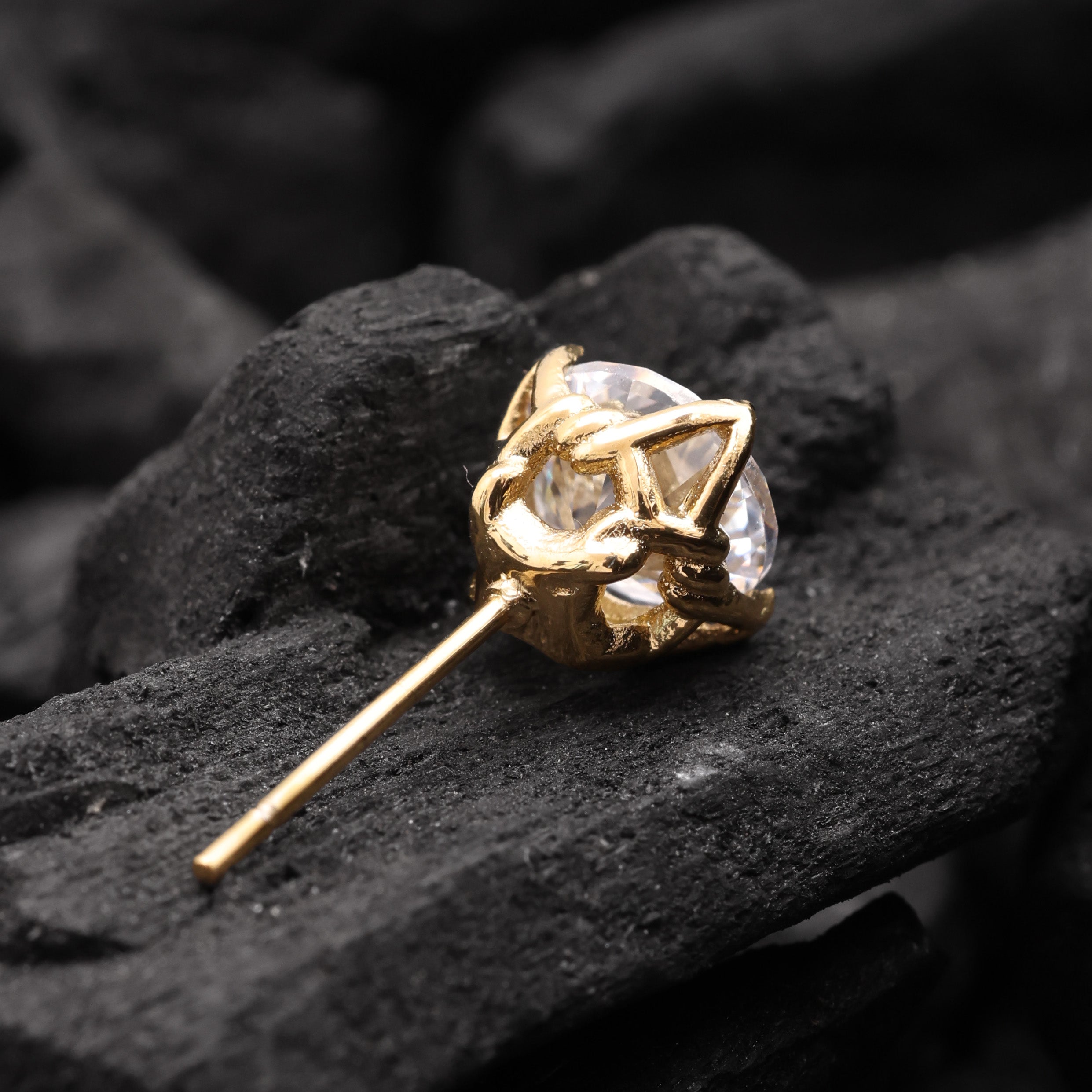 Gold earring with a clear gemstone on black stone surface
