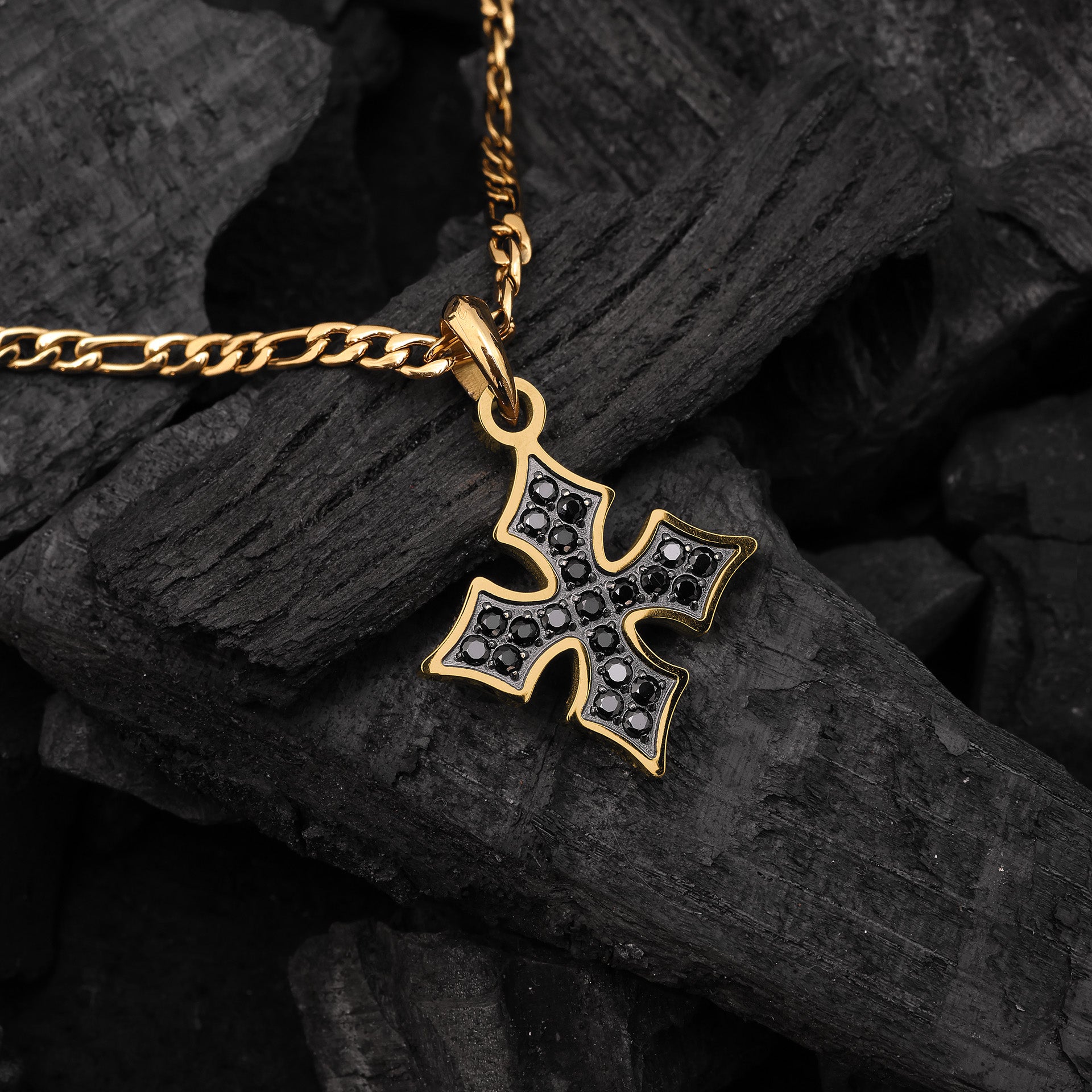 Gold cross pendant necklace with black zircon stones on a dark stone surface