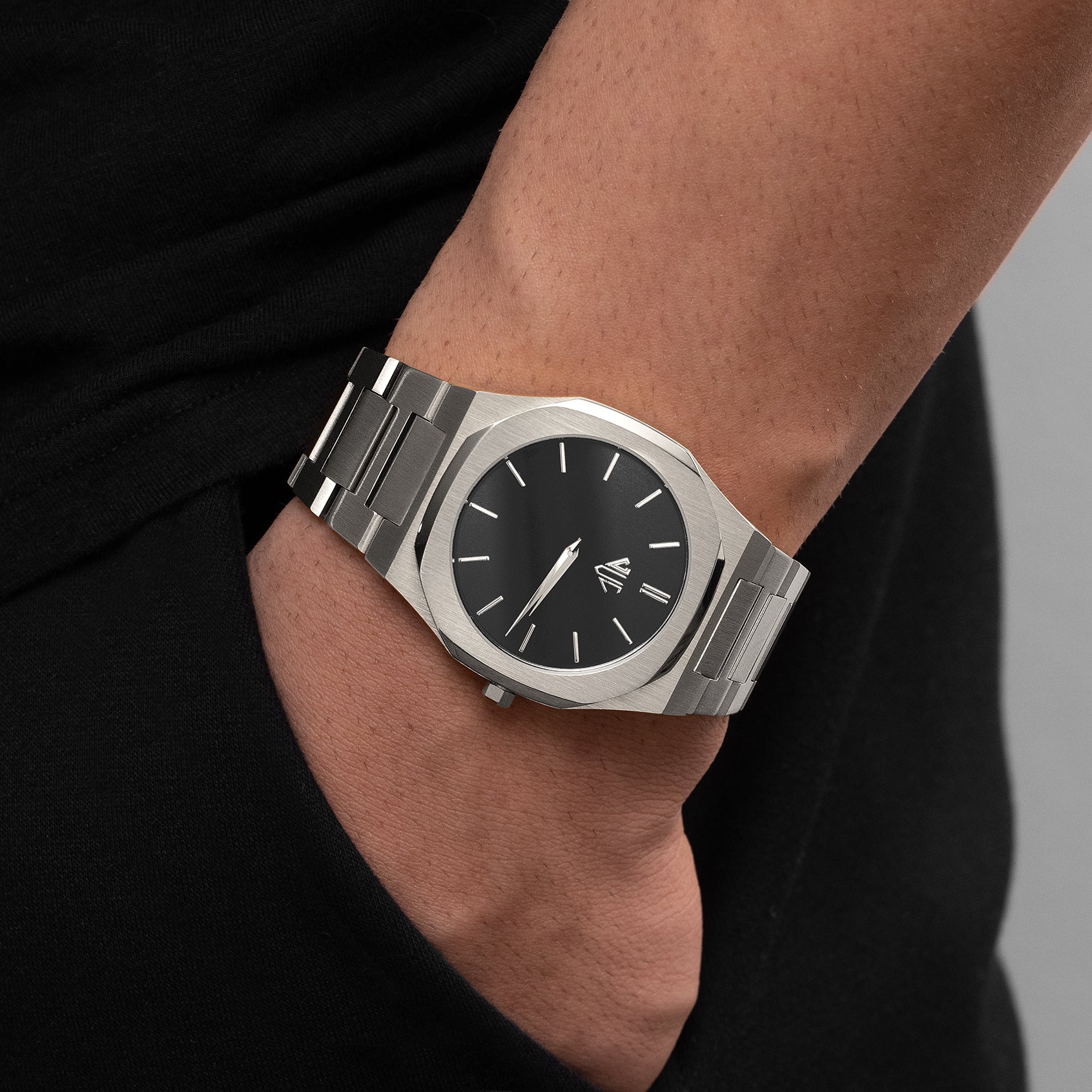 Silver watch with black dial on a wrist against a neutral background 