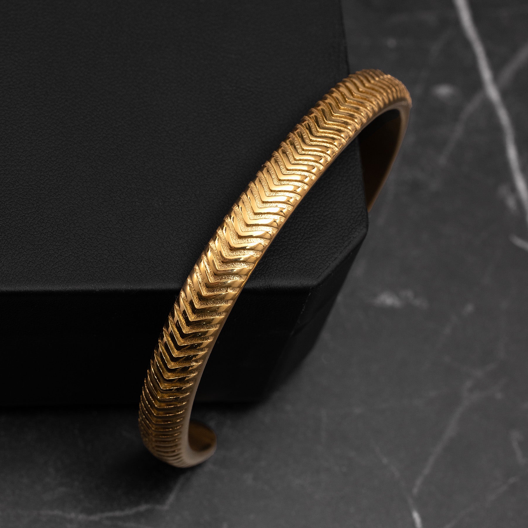 Gold bracelet with a textured pattern on a dark background